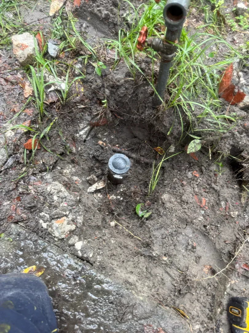 Close-up of a capped pipe stub at the bottom of an excavated hole beside a metal standpipe