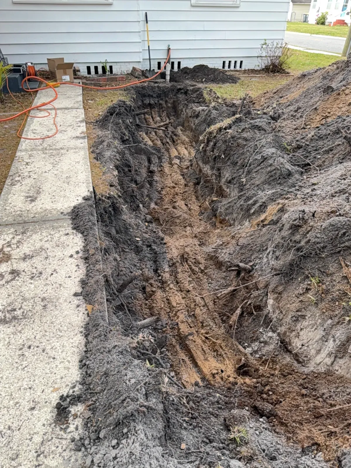 Open trench dug beside a front walkway, running from the house foundation toward the street