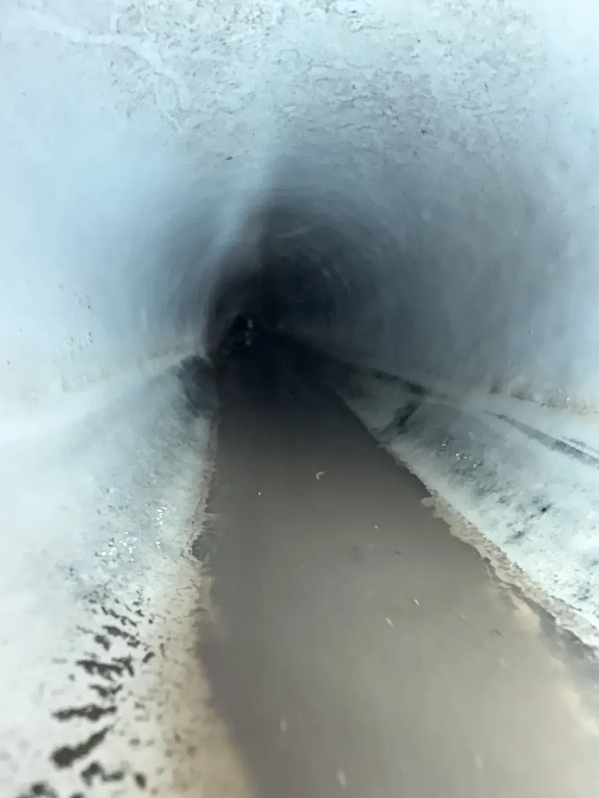 Sewer camera view inside a buried drain pipe with water sitting along the bottom