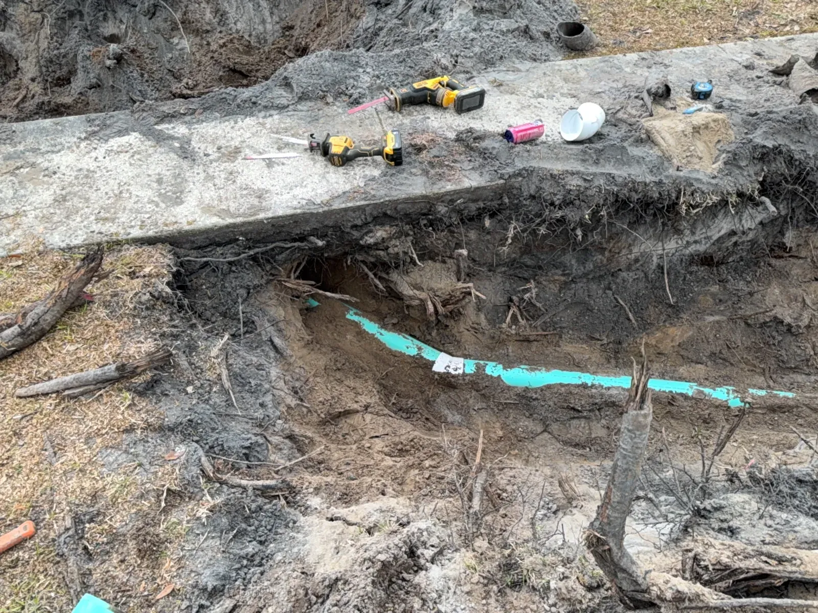 New green PVC sewer line in a trench beside a walkway, with power tools and fittings on the slab