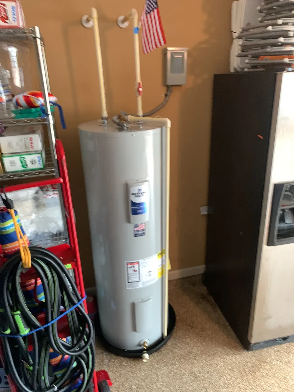Electric water heater on a drain pan in a garage with new supply lines, photo slightly blurred